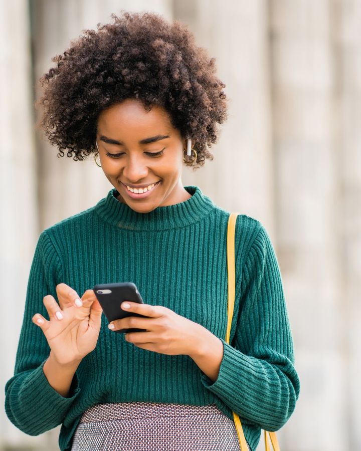 Una mujer sonríe mientras escribe en su celular